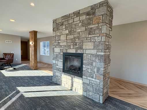 A stone fireplace in a room with a grey carpet.