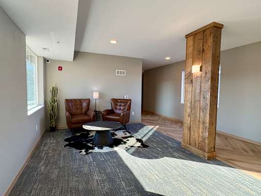 A room with a wooden column and two brown leather chairs.