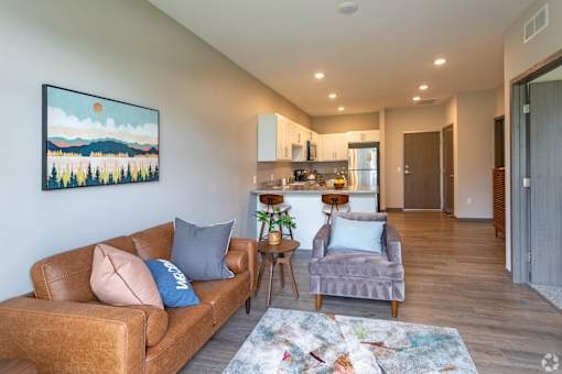 A living room with a brown couch and a painting of a landscape on the wall.