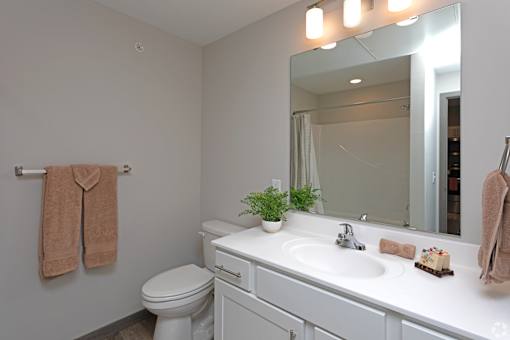 A bathroom with a toilet, sink, mirror, and towel rack.