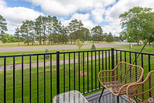 A balcony with a black railing, a wicker chair and a table.