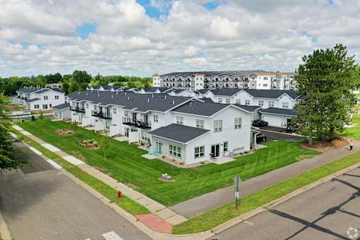 A large white building with a black roof is surrounded by a green lawn.