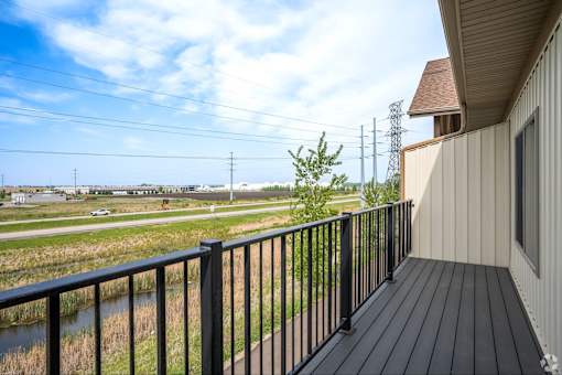 A balcony with a black railing overlooks a field with power lines in the distance.
