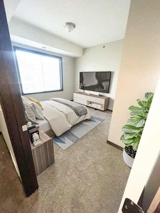A bedroom with a bed, nightstand, and a TV on the wall.