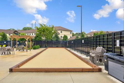 A shuffleboard court is located in a courtyard surrounded by chairs and a fence.