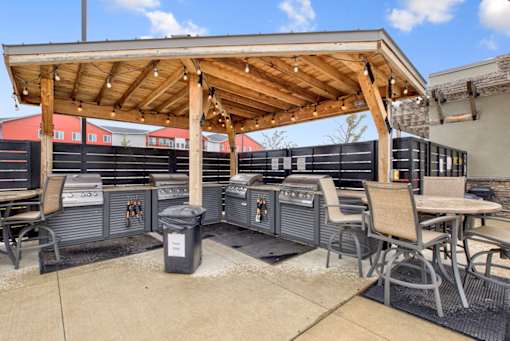 A patio with a grill and chairs under a wooden roof.