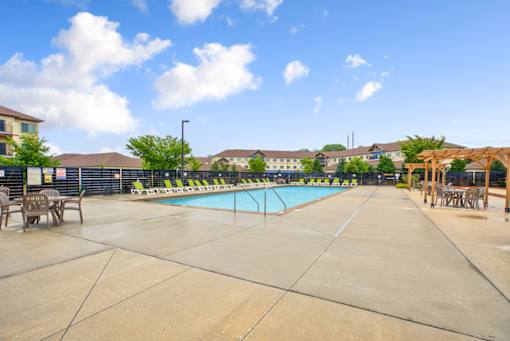 A large outdoor swimming pool surrounded by a concrete patio and lounge chairs.