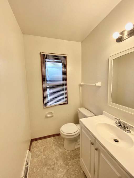 A white bathroom with a toilet, sink, and window at Root River Apartments, Wisconsin