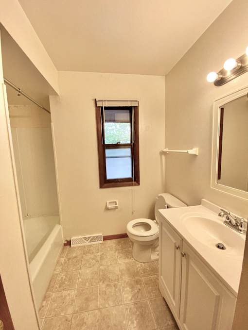 A bathroom with a toilet, sink, and a window at Root River Apartments, Greendale, 53129