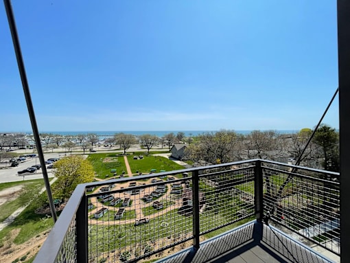 A balcony overlooks a parking lot and a green field.