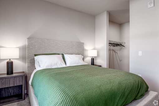 A bed with a green blanket and white pillows in a room with a lamp at Bloom, Monona, 53716