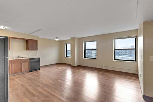 A room with wooden floors and a kitchen area with a refrigerator, microwave, and cabinets.