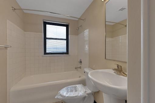 A white sink is in a bathroom with a white tub and a window.