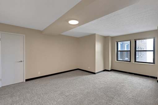 A room with a carpeted floor and a window with a view of a street.