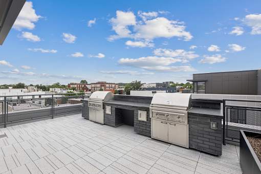 A rooftop patio with a grill and a table.