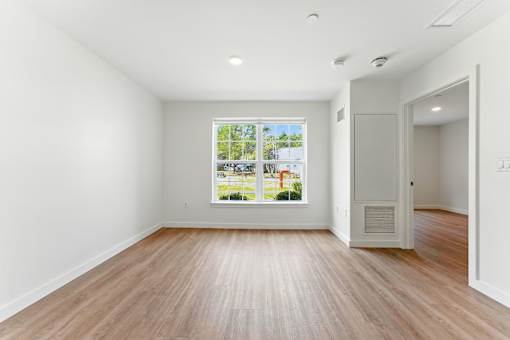 A room with wooden floors and a large window showing a view of a street with houses.