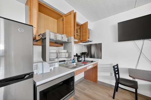 A kitchen with a refrigerator, microwave, oven, sink, and a chair.