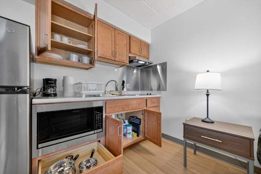 A kitchen with a refrigerator, microwave, oven, sink, and a table with a lamp.