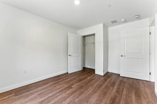 A room with white walls and wooden flooring with three doors.