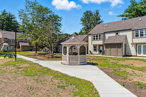 A gazebo is in the middle of a grassy area in front of apartment buildings.