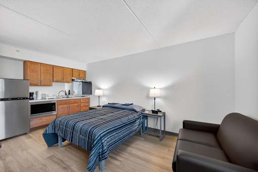 A bedroom with a bed, a couch, and a kitchen area.
