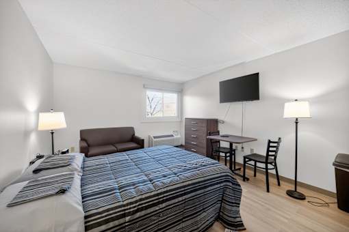 A bedroom with a bed, desk, chair, and a television.