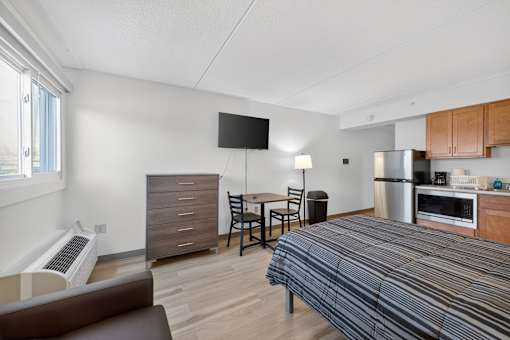 A bedroom with a bed, a couch, a chair, a table, a microwave, and a refrigerator.