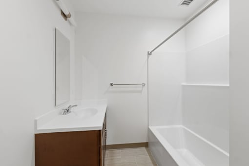A white bathroom with a sink, mirror, and bathtub.