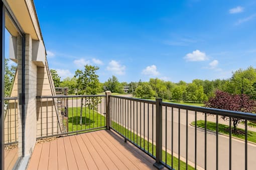 A balcony with a black railing overlooks a green lawn and trees.