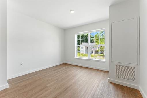 A room with a window showing a view of a house and trees outside.