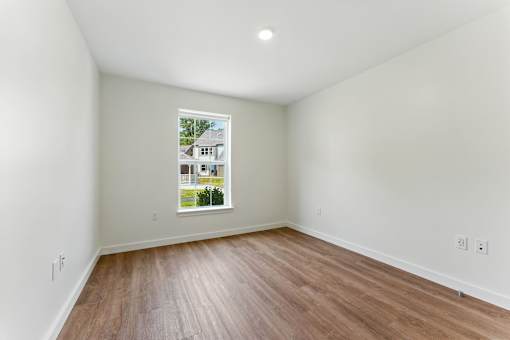 A room with wooden floors and a window showing a house across the street.