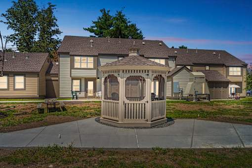 A gazebo is in the middle of a concrete patio in front of a house.