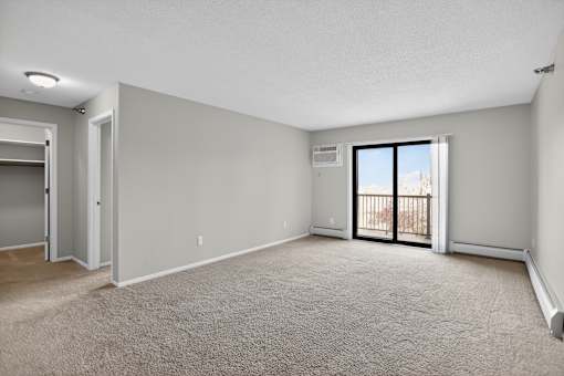 A spacious room with a carpeted floor and a sliding glass door leading to a balcony.