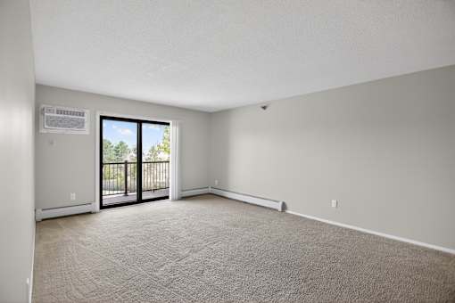 A room with a carpeted floor and a sliding glass door leading to a balcony.