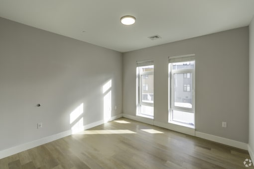 an empty living room with two windows and a wood floor