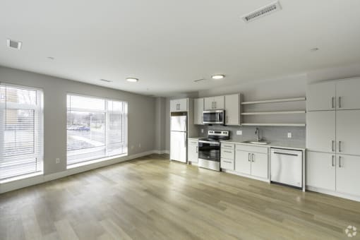 an empty kitchen with white cabinets and appliances and a large window