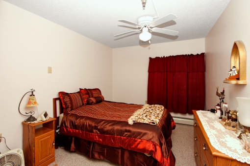 A bedroom with a bed, dresser, and ceiling fan.