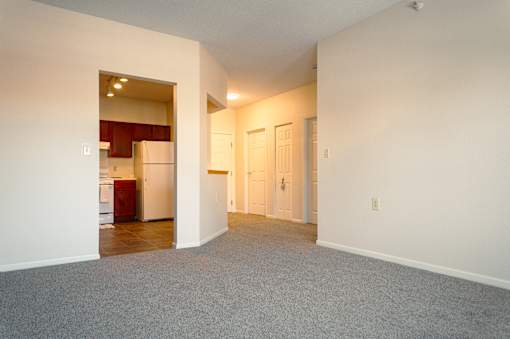 A large empty room with a kitchen visible through the open door.
