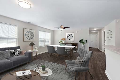 A living room with a grey sofa, a grey armchair, a wooden coffee table, a white dining table, and a ceiling fan.