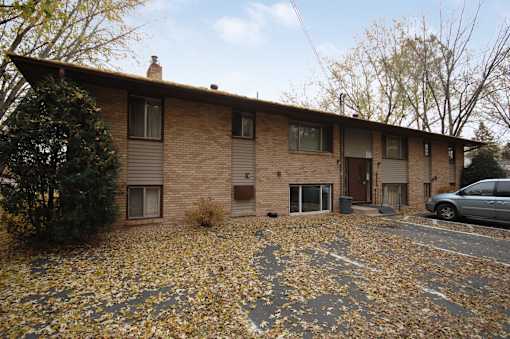 A house with a brown brick exterior and a grey roof with a car parked in front.
