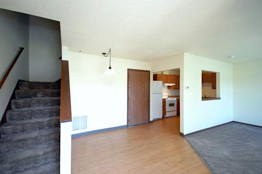 A room with a staircase on the left and a kitchen area on the right.