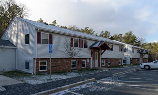 A building with a red brick wall and a white siding with a car parked in front.