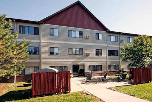 A large apartment building with a red roof and a fence in front.