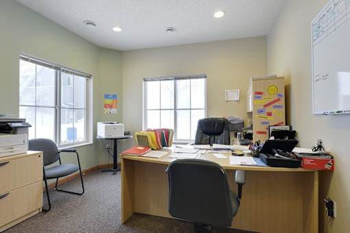 A whiteboard is on the wall in an office with a desk and chairs.