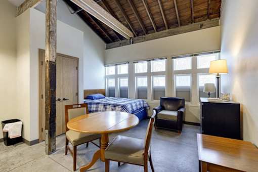 A room with a bed, a chair, a table, and a lamp.