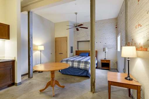 A bedroom with a bed, a table, and a ceiling fan.