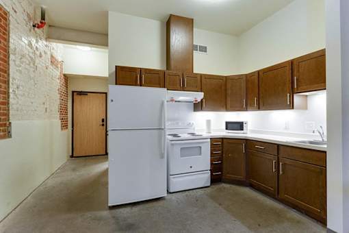 A kitchen with a white refrigerator, wooden cabinets, and a brick wall.
