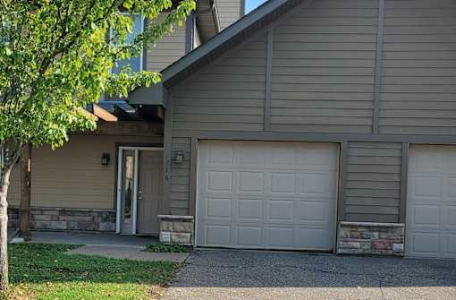 A house with a grey garage door and a tree in front.
