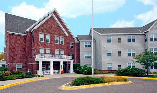 A red brick building with a white porch and a grey building to the right.