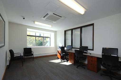 A room with a desk, chairs, and computers.